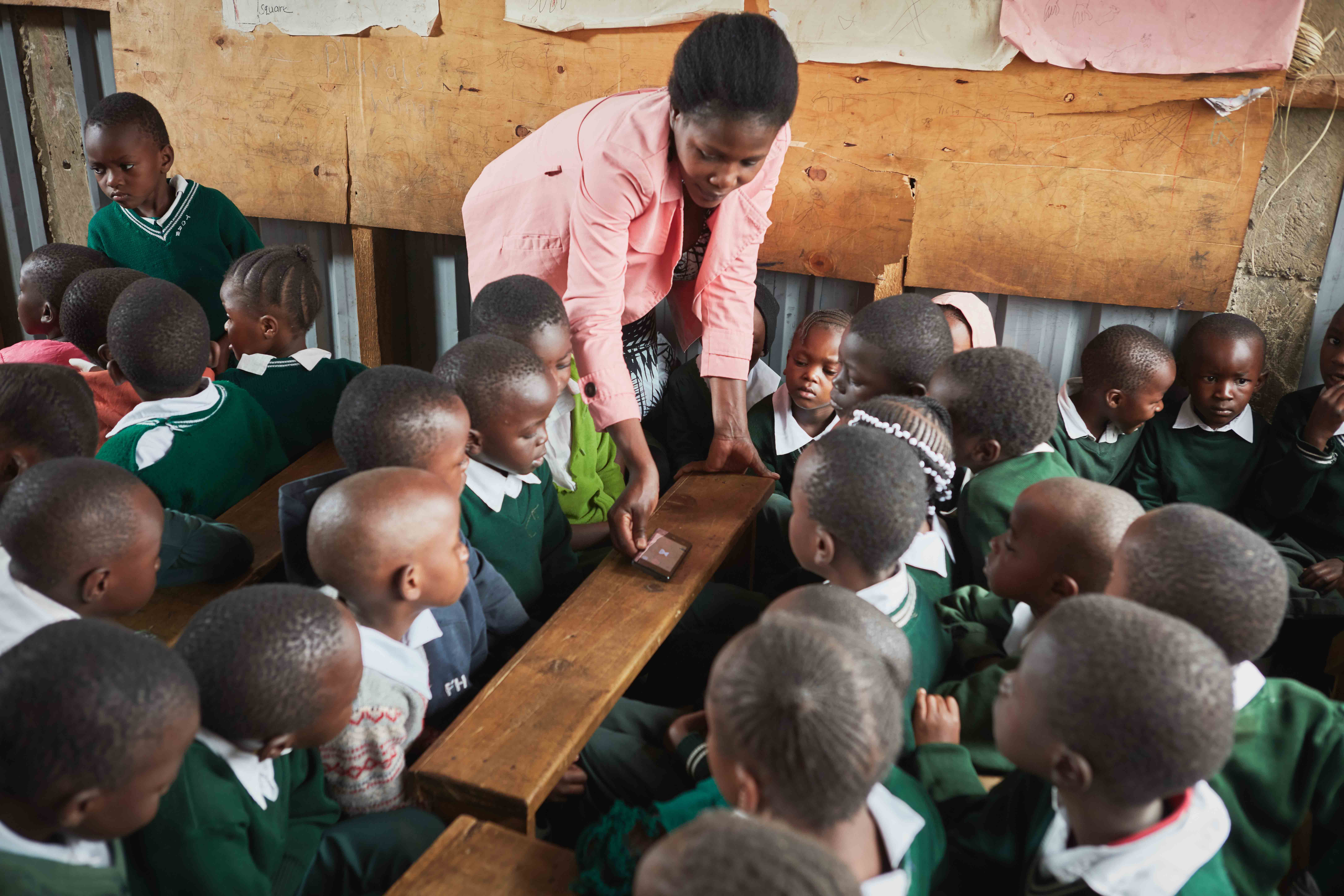 A teacher in Kenya wearing a pink blouse interacts with her students while using the EIDU app in the classroom.