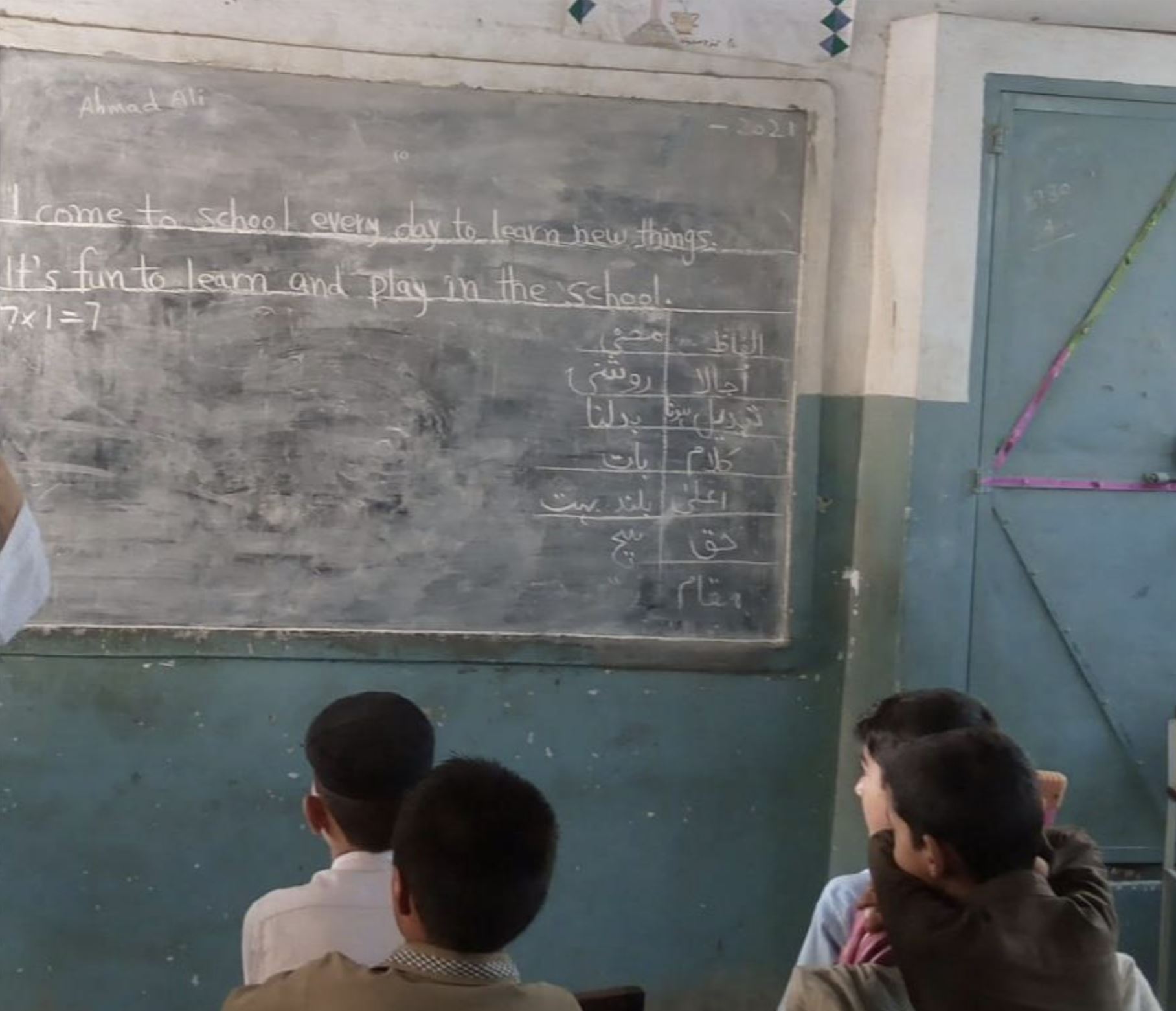 Children in school looking at whiteboard that shows the message 'I come to school every day to learn new things' written in chalk